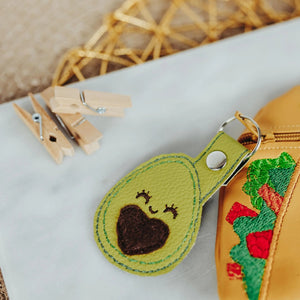 TACO KAWAII ZIPPERED POUCH FOR KIDS Tiny Owls Gift Co Close up of green avacado keychain on white tray beside three wooden clothes pins