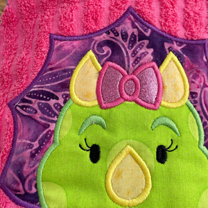 Green and purple dinosaur with a pink bow on a pink and purple patterned background