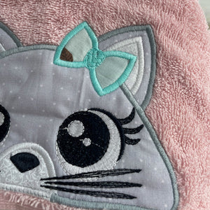 Embroidered cat face patch with a bow on a pink fabric background