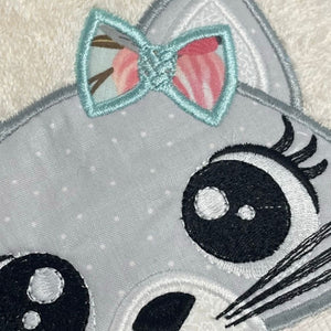 Embroidered patch of a cat face with a bow on a gray background