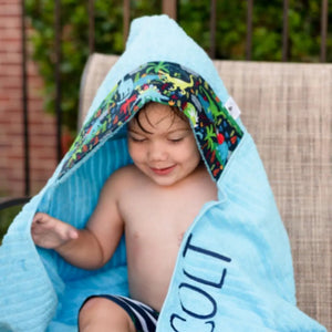 Boy wearing a blue hooded towel with a dinosaur fabirc trim