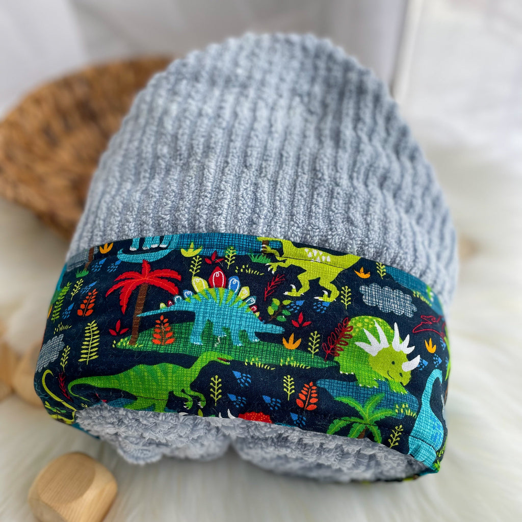 Light blue hooded towel with colorful dinosaur pattern on a white surface