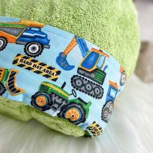 Lime Green Hooded towel folded with a pale blue fabric featuring tractors dump trucks loader and backhoes close up