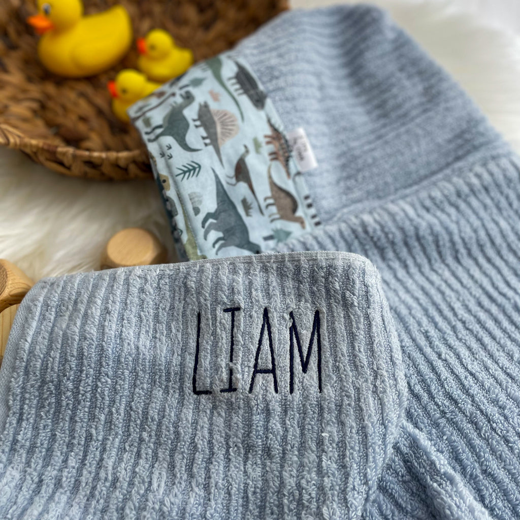 Blue towel with 'LIAM' embroidered on it, folded against a neutral background.