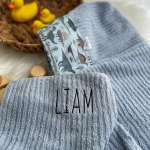 Blue towel with 'LIAM' embroidered on it, folded against a neutral background.