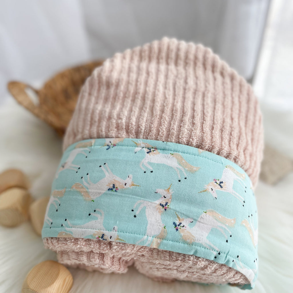 Pale pink hooded towel with light blue trim featuring white unicorns