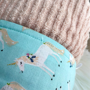 Close up of a Pale pink hooded towel with light blue trim featuring white unicorns