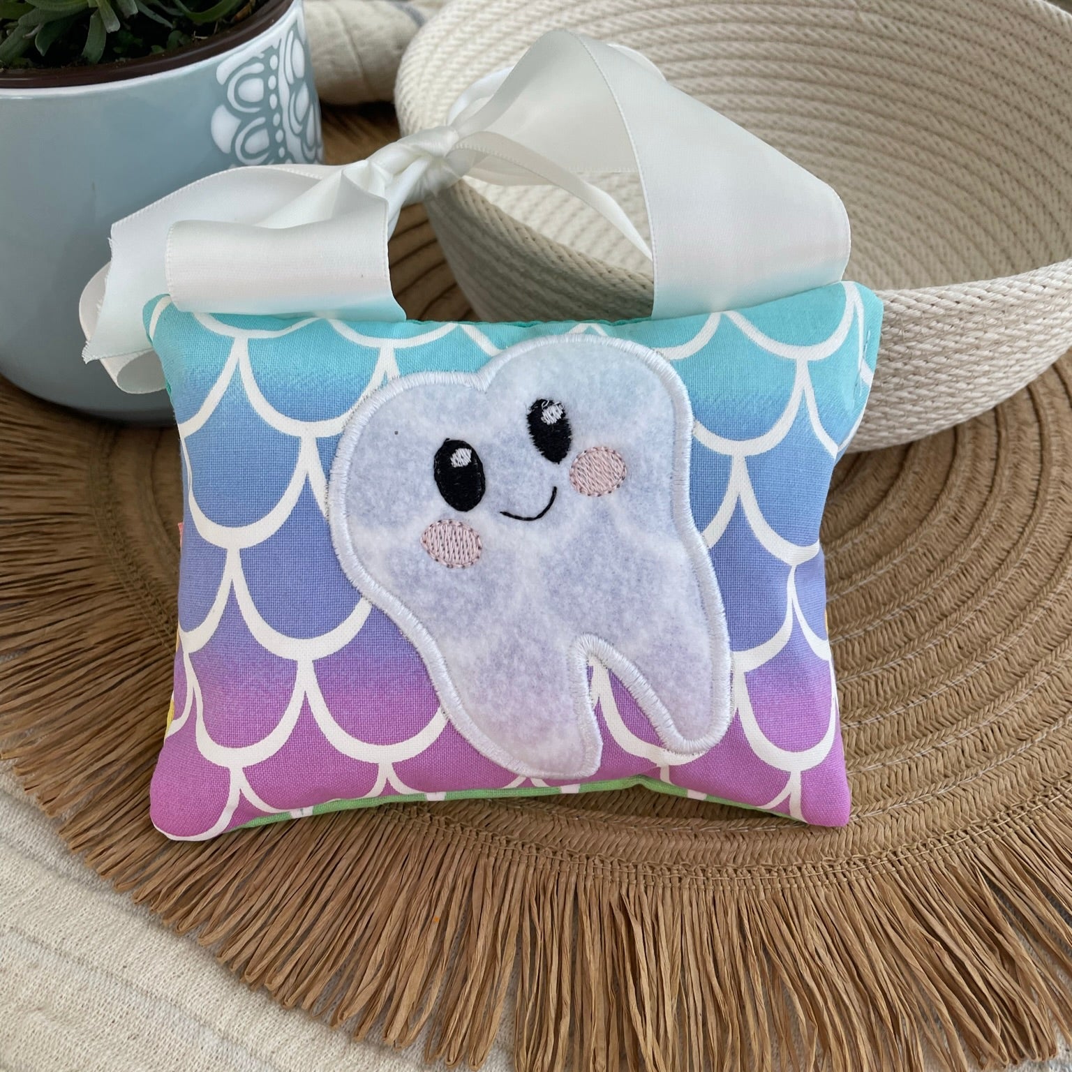 tooth fairy pillow with mermaid scales sitting on placemat in front of bowl an d flower pot