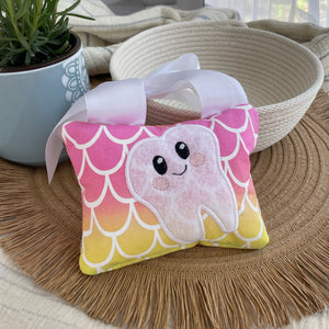 tooth fairy pillow with mermaid scales sitting on placemat in front of bowl an d flower pot