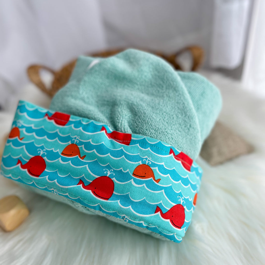 Turquoise towel with orange whale pattern on a white surface