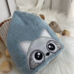 Raccoon face appliqued on a blue towel hood sitting on a white background