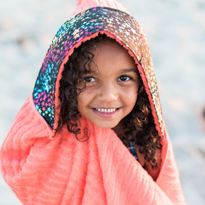 Child wearing a coral hooded towel with a rainbow stars fabric trim