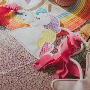 Rainbows & Unicorns Birthday Banner laying on a sequin tablecloth with a rainbow placemat Tiny Owls Gift Co