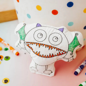 monster doodle pillow partially colored leaning on a polka dot pot with google eyes and markers surrounding