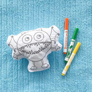 round monster coloring pillow on blue towel with orange green and yellow washable markers beside