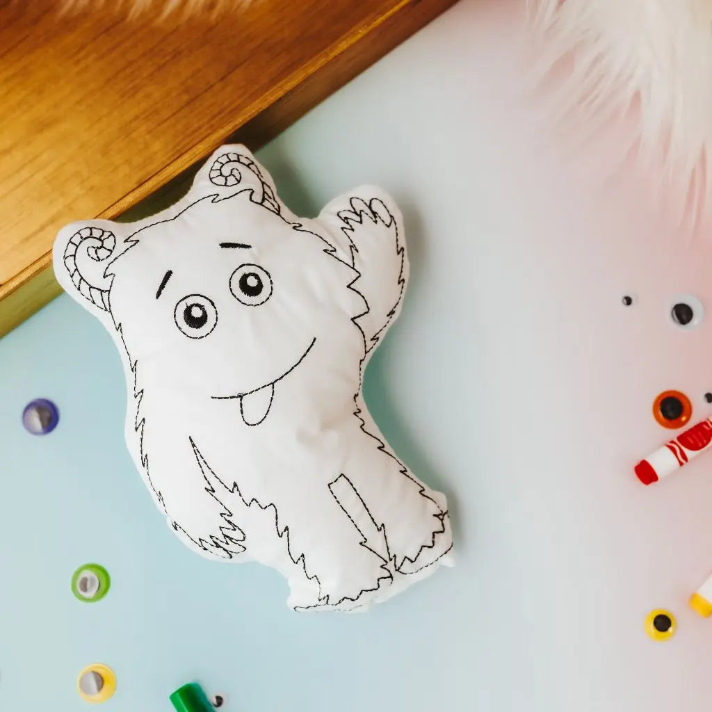 Silly Monster Coloring Doll & Party Favor laying on a blue sheet with colored google eyes and markers surrounding