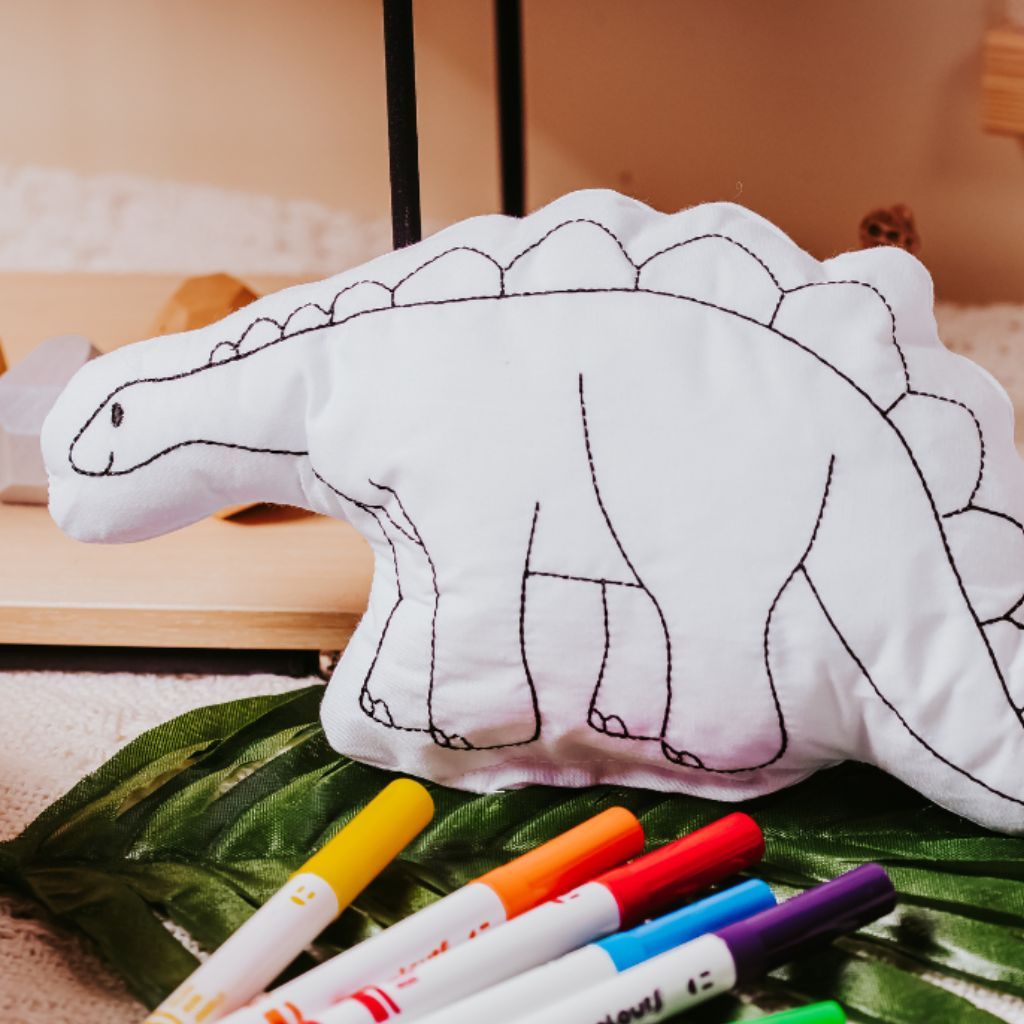 Tiny Owls Gift Co stegosaurus doodle pillow sitting on leaf with washable markers in front
