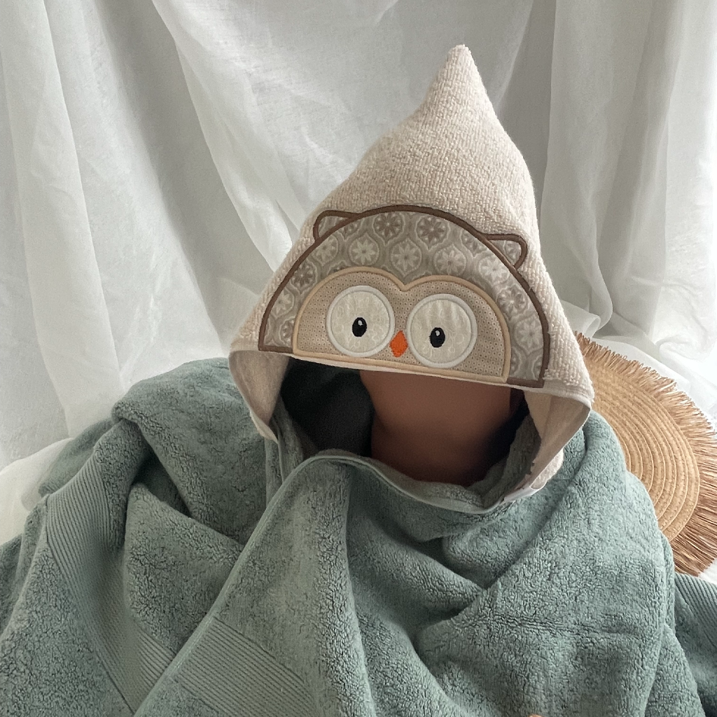 kids hooded towel with an owl design against a white curtain background
