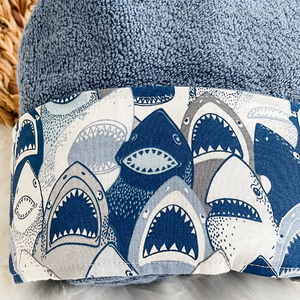 blue towel with a fabric trim featuring toothy shark faces in shades of blue grey and white