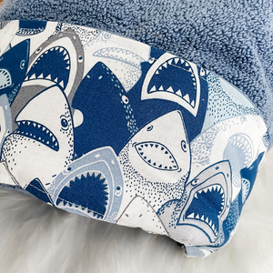blue towel with fabric trim featuring toothy shark faces on a white surface