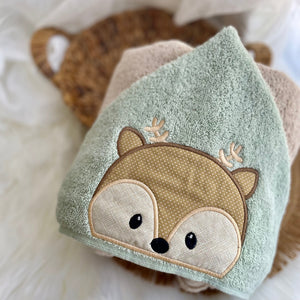 woodland baby deer face on a green hood of a tan hooded towel on a white surface