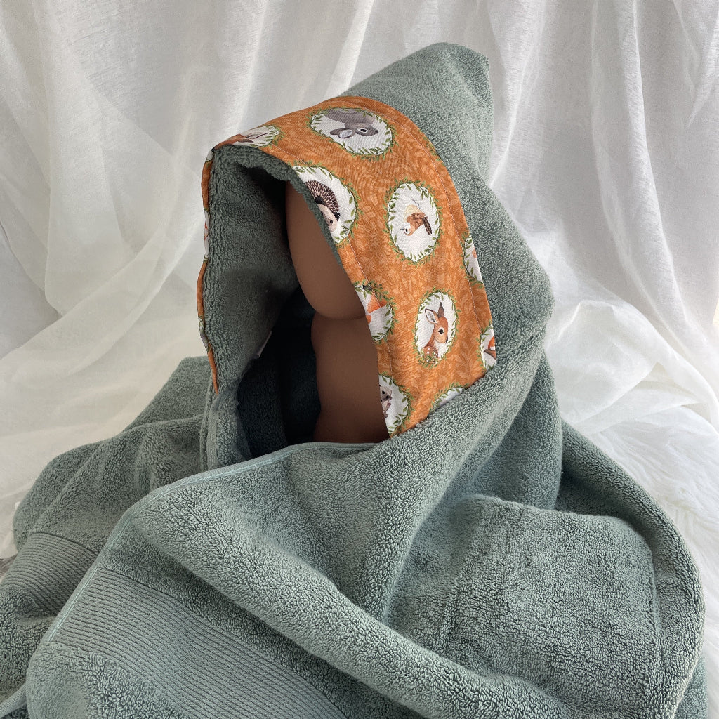 sage green hooded towel with an orange band of fabric with woodland animals